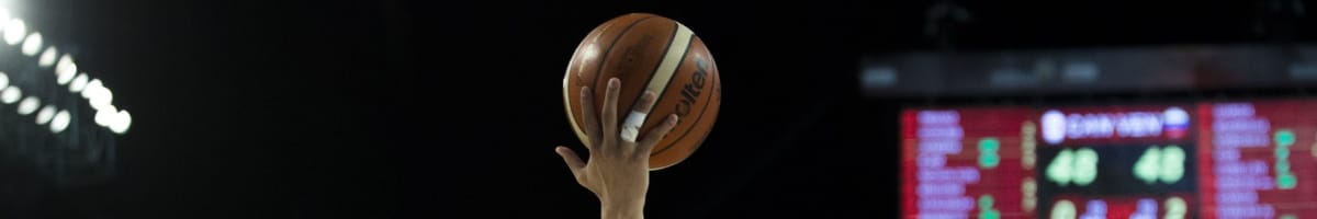 Player’s hand lifts basketball in dark background.