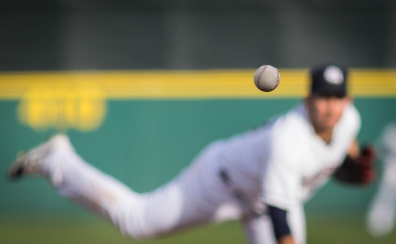 A baseball in motion with pitcher in background.