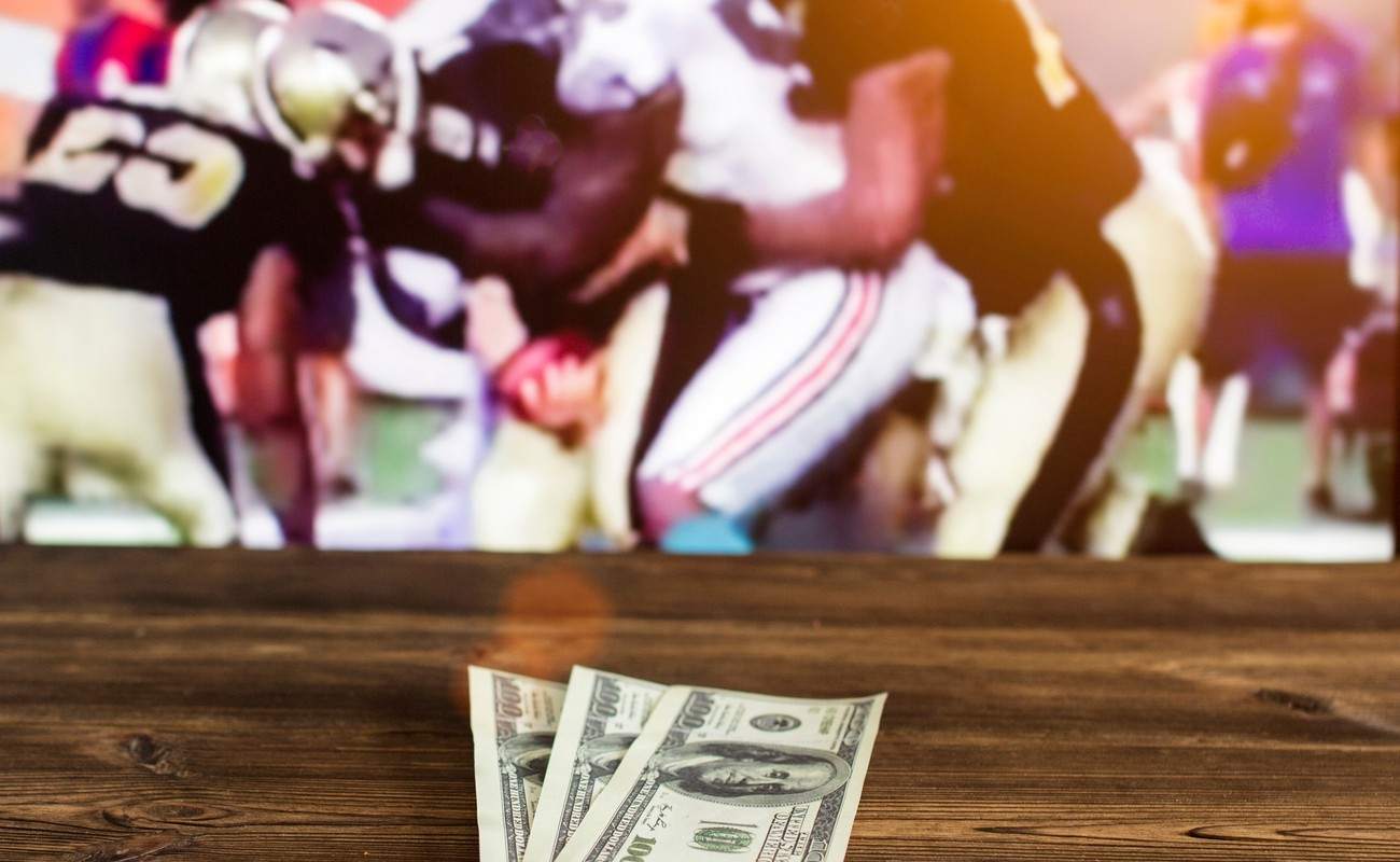  Dollars on a wooden table with a TV in the background showing American football