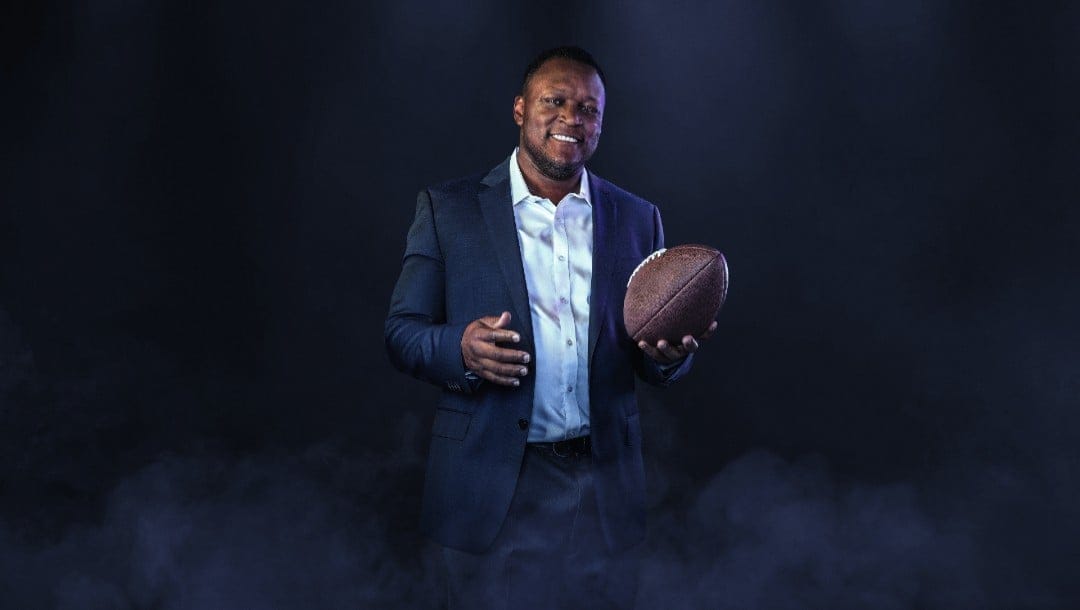 Former NFL player Barry Sanders holding a football on a dark background