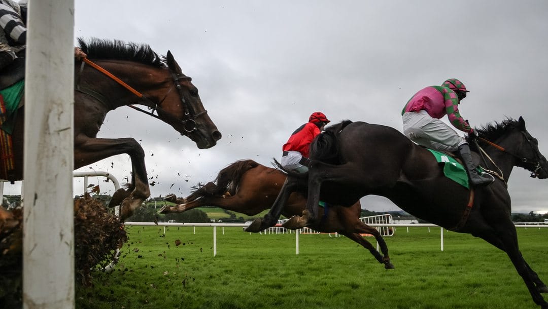 Several horses clear a jump during a steeplechase race.