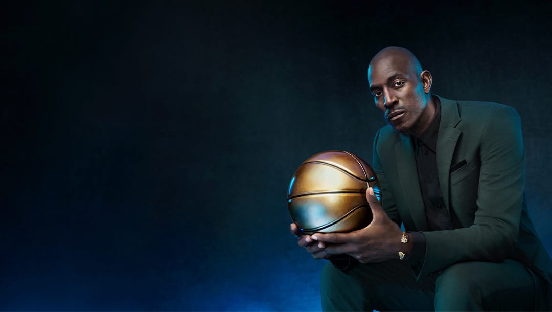 Former NBA player Kevin Garnett holding a golden basketball on a dark blue background.