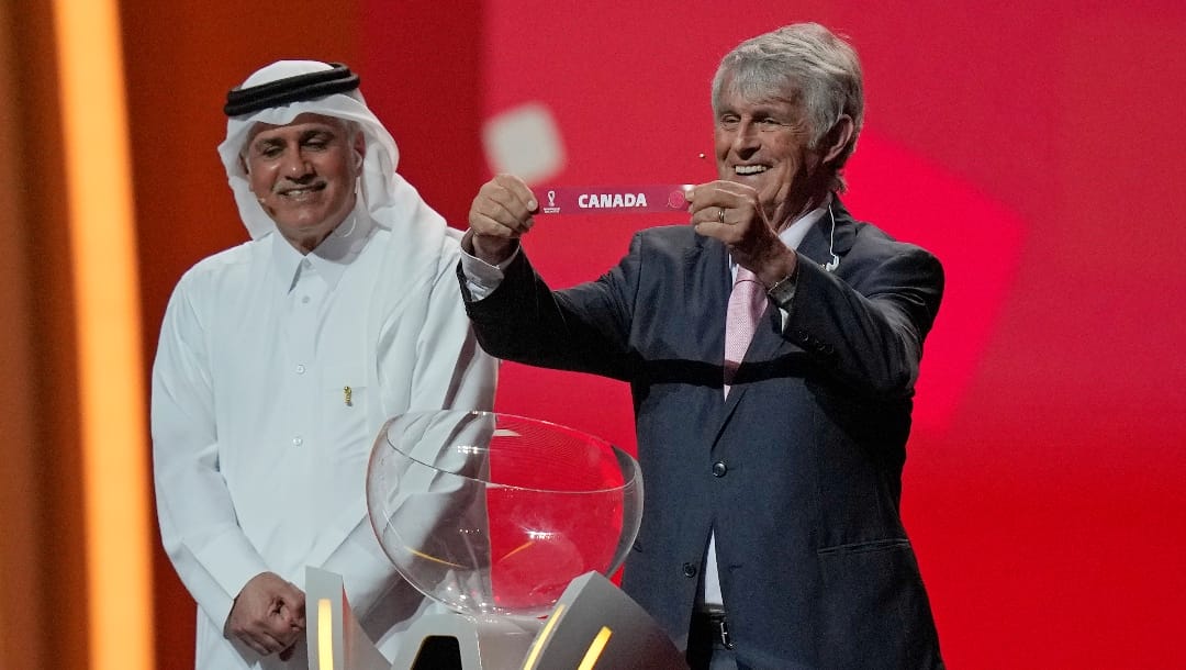 Serbian-Mexican retired soccer manager Bora Milutinovic holds up the name of Canada as he assists in the 2022 soccer World Cup draw at the Doha Exhibition and Convention Center in Doha, Qatar, Friday, April 1, 2022. (AP Photo/Darko Bandic)