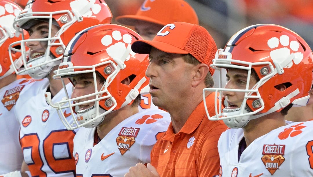 FILE - Clemson head coach Dabo Swinney, second from right, walks with players on the field before the Cheez-It Bowl NCAA college football game against Iowa State, Wednesday, Dec. 29, 2021, in Orlando, Fla. The perpetually positive Swinney probably has more need for it these days with his team breaking in three new assistants including first-time Clemson coordinators on defense in Wes Goodwin and offense in Brandon Streeter.