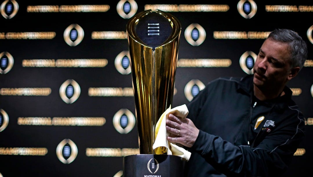FILE - In this Jan. 7, 2018 file photo Charley Green buffs the NCAA college football championship trophy before a coaches news conference in Atlanta. The College Football Playoff selection committee begins its fifth season Tuesday, Oct. 30, 2018 of presenting weekly rankings and if form holds two schools in the first top four will go on to play in the semifinals. The usefulness of the committee’s work and the nationally televised reveal is debatable. But what if anything can be learned from the first four years of CFP rankings? Of the 16 teams the committee ranked in the top four of its initial rankings from 2014-17, half made the playoff. (AP Photo/David Goldman, file)