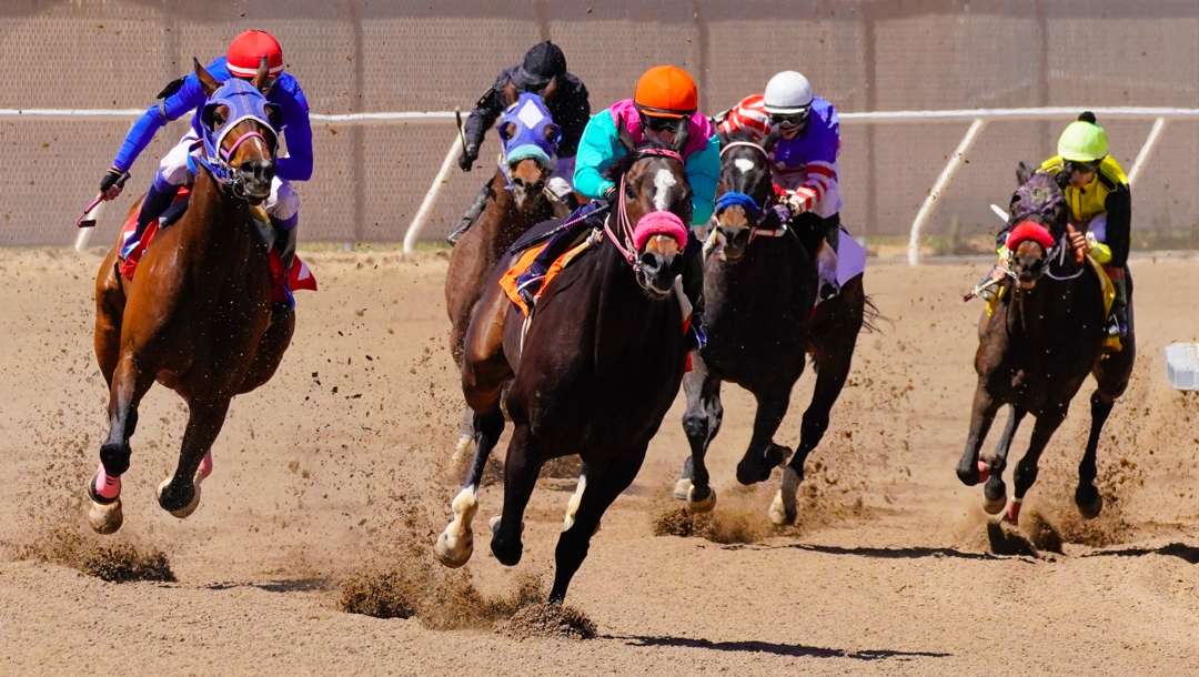 Horses and their jockeys racing on a dirt track.