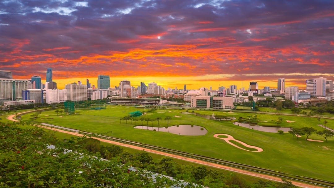 A racetrack going around a golf course with a cityscape in the sunset.