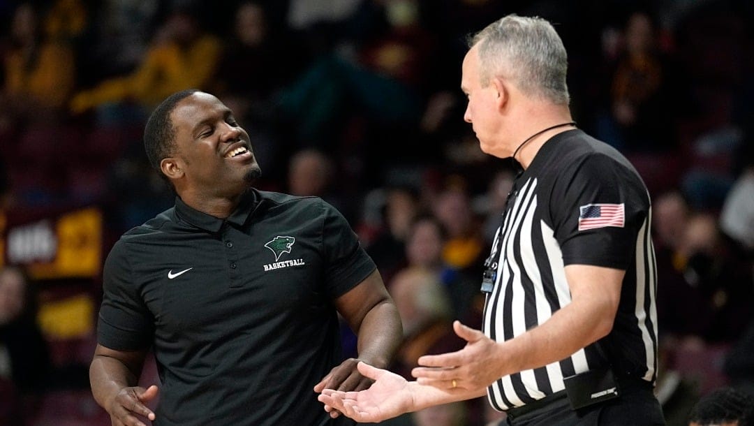 A coach with a black shirt is talking and laughing with an umpire dressed in black and white striped uniform