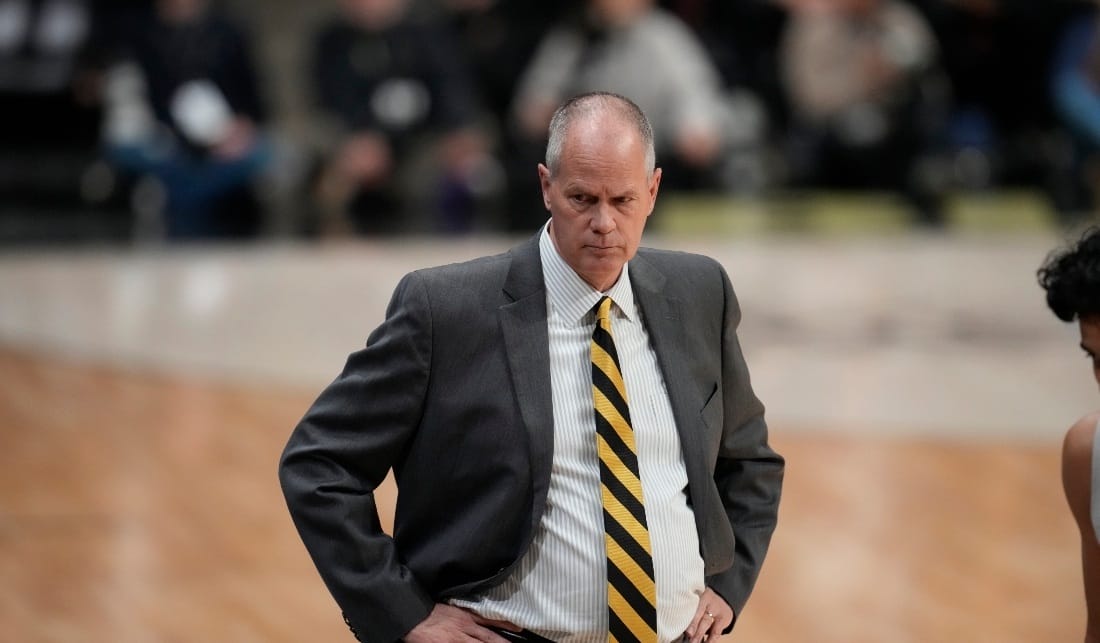 A team manager dressed in a suit and a yellow and black striped tie, looking worried.