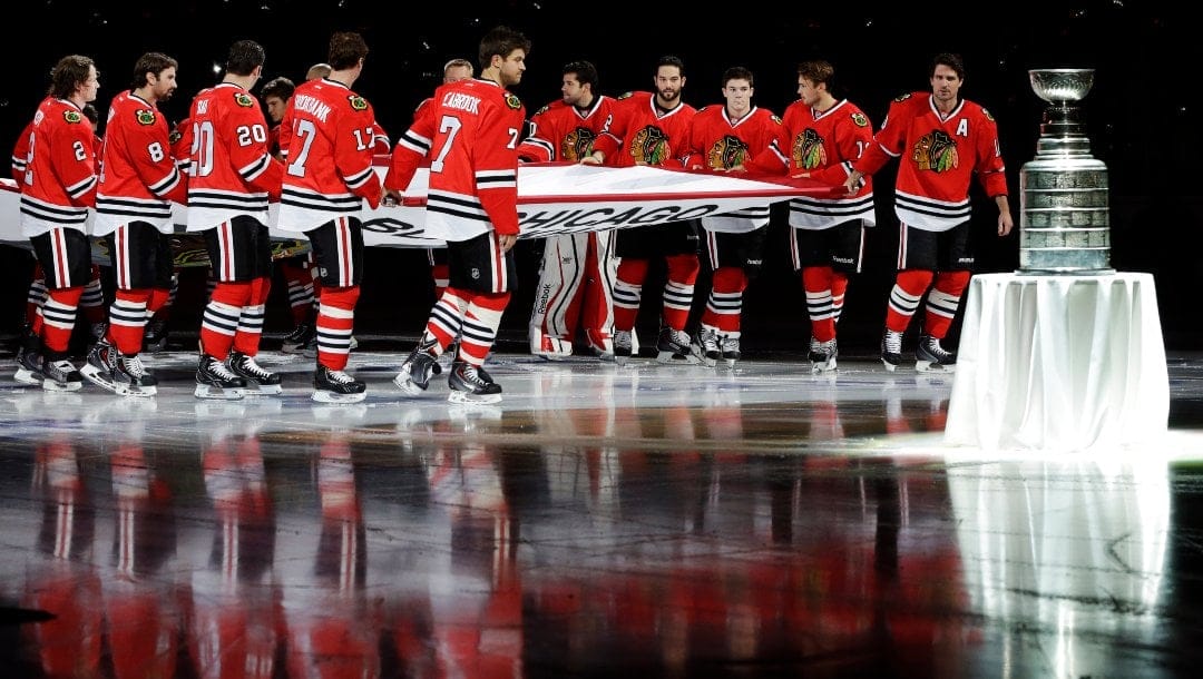 The Chicago Blackhawks players carry out the Stanley Cup Championship banner past the Stanley Cup during a ceremony before an NHL hockey game between the Blackhawks and the Washington Capitals on Tuesday, Oct. 1, 2013, in Chicago.