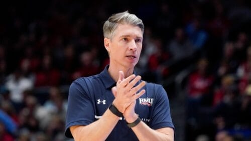 A coach with a blue team shirt is watching the game and clapping his hands