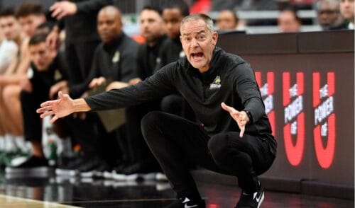 A coach dressed in Black hunching and indicating gameplay with his hands while shouting