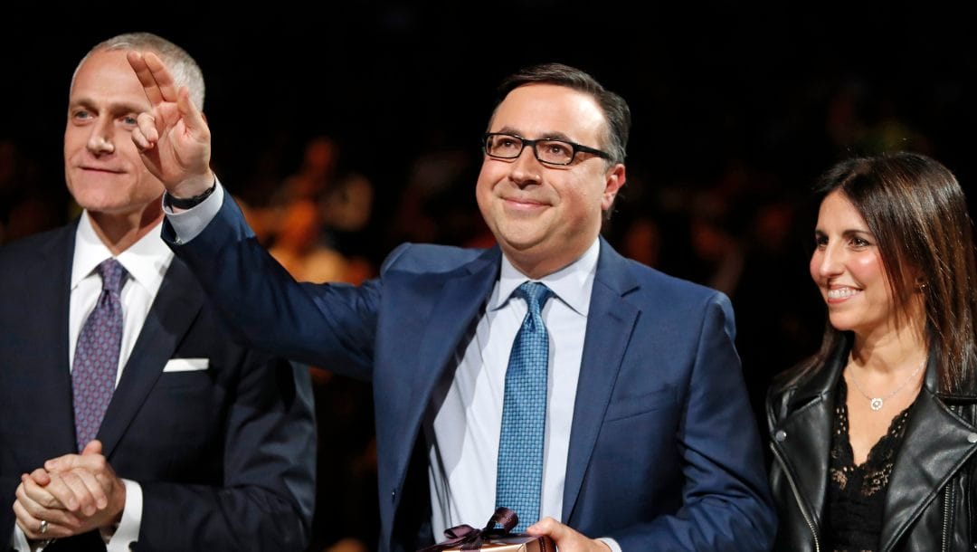 Brooklyn Nets Nets broadcaster Ian Eagle , center, waves to the crowd as Nets' CEO Brett Yormark, left, applauds during a ceremony honoring Eagle's 25-year broadcast career at an NBA basketball game between the New York Knicks and the San Antonio Spurs, Thursday, Feb. 21, 2019, in New York. Eagle's wife Amy is at right.