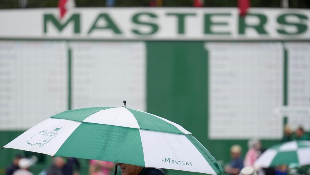 A spectator walks in the rain past the main leaderboard during the first round at the Masters golf tournament on Thursday, April 7, 2022, in Augusta, Ga.