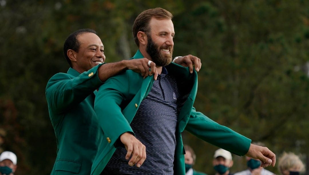 Tiger Woods helps Masters’ champion Dustin Johnson with his green jacket after his victory at the Masters golf tournament Sunday, Nov. 15, 2020, in Augusta, Ga. (AP Photo/Charlie Riedel)