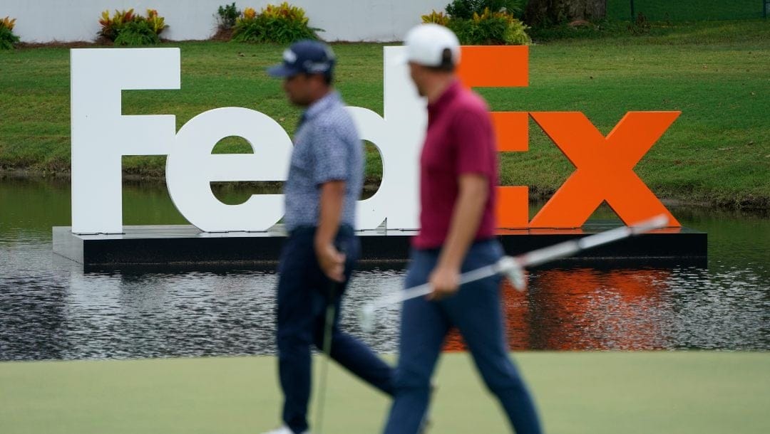 Players walks past a FedEx sign during the first round of the St. Jude Championship golf tournament Thursday, Aug. 11, 2022, in Memphis, Tenn.