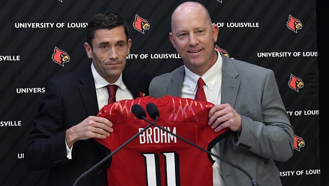Louisville athletic director Josh Heard, left, presents newly named football coach Jeff Brohm with a jersey in Louisville, Ky., Thursday, Dec. 8, 2022. The arrivals of Brohm and Georgia Tech's Brenty Key this year mean that nearly half the ACC's coaches have turned over in the past two seasons, compared to the 2021 season when all 14 football coaches returned to the job.