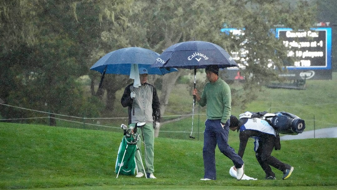 Marcel Siem, of Germany, second from left, uses an umbrella to shield from the rain while on the 16th green of the Pebble Beach Golf Links during the third round of the AT&T Pebble Beach Pro-Am golf tournament in Pebble Beach, Calif., Sunday, Feb. 5, 2023.