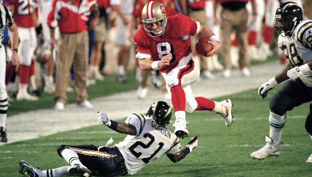 In this Jan. 29, 1995, file photo, San Francisco 49ers' quarterback Steve Young (8) runs over San Diego's Darrien Gordon (21) for a first down during the first quarter of Super Bowl XXIX at Joe Robbie Stadium in Miami. The NFL became a truly booming business in the 1990s, with multi-billion-dollar TV contracts, expansion to 30 teams, and a late-decade wave of new stadiums. Players began to pick up a bigger share of the wealth, with the dawn of unrestricted free agency. The results on the field were largely dominated by the NFC, with Emmitt Smith and the Dallas Cowboys, Young and the 49ers, and Brett Favre and the Green Bay Packers enjoying the most success.