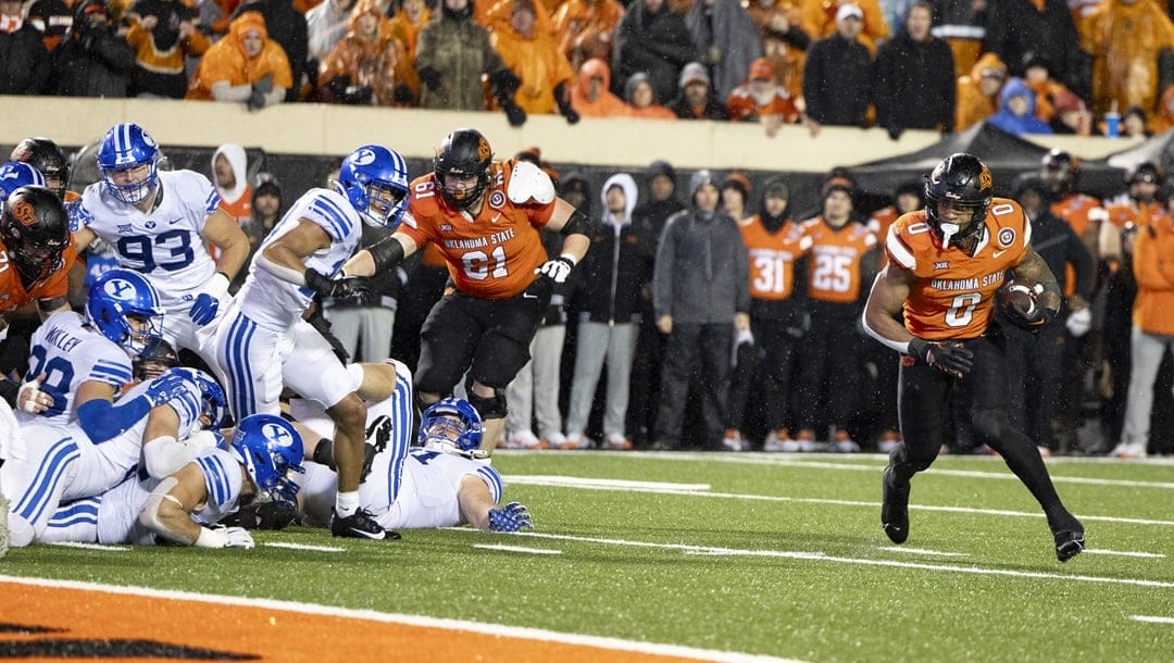 Oklahoma State running back Ollie Gordon II (0) runs past BYU defenders for a touchdown in the first halftime of an NCAA college football game Saturday, Nov. 25, 2023, in Stillwater, Okla.