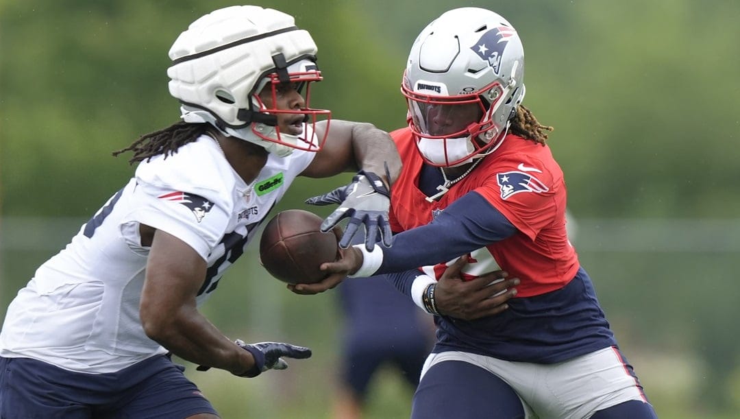 New England Patriots quarterback Joe Milton III, right, hands off to New England Patriots running back Deshaun Fenwick, left, during an NFL football training camp, Wednesday, July 24, 2024, in Foxborough, Mass.