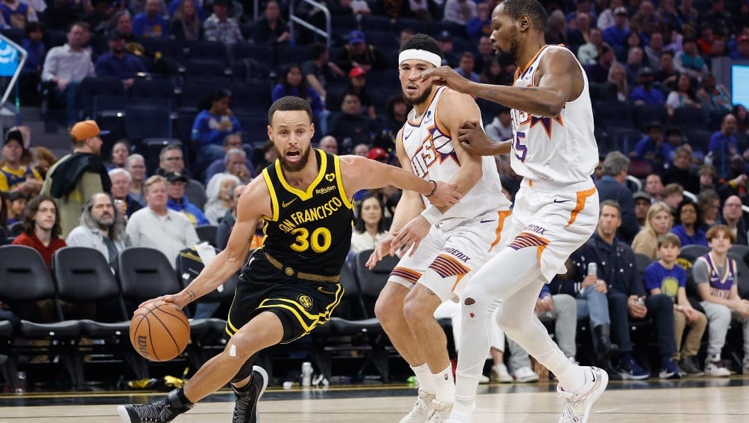 : Stephen Curry #30 of the Golden State Warriors drives to the basket against Devin Booker #1 and Kevin Durant #35 of the Phoenix Suns in the third quarter at Chase Center on February 10, 2024 in San Francisco, California.