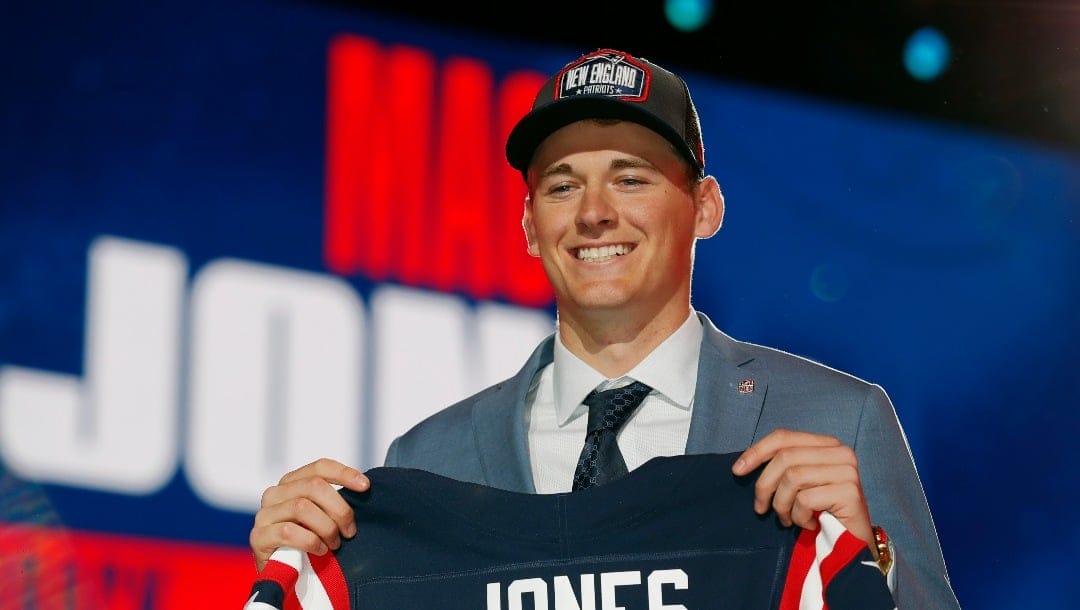 Alabama quarterback Mac Jones holds a team jersey after he was by the New England Patriots during the first round of the NFL football draft, Thursday April 29, 2021, in Cleveland.