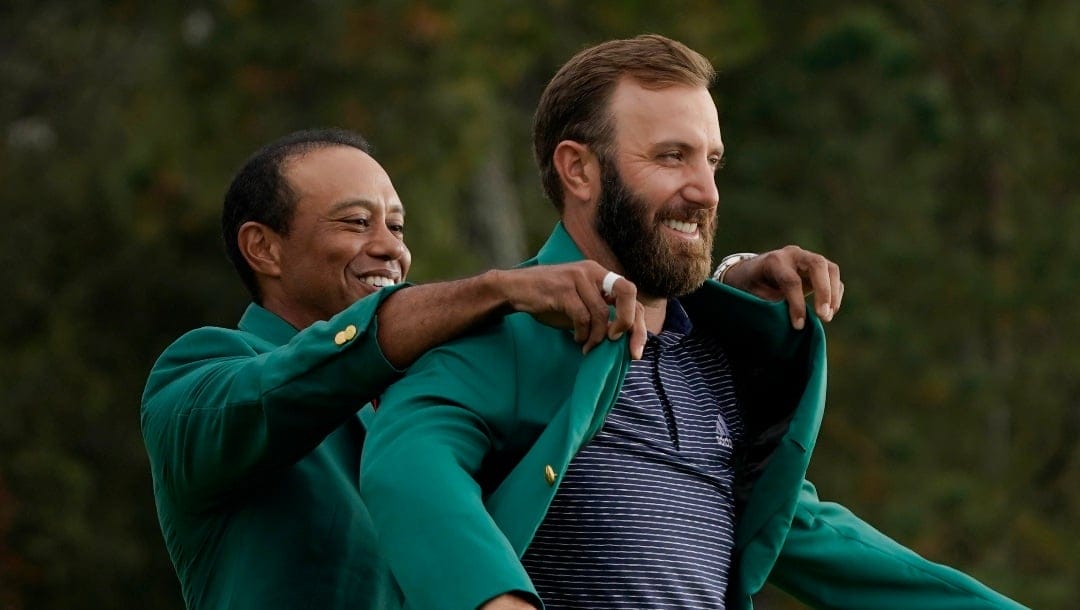 Tiger Woods helps Masters’ champion Dustin Johnson with his green jacket after his victory at the Masters golf tournament Sunday, Nov. 15, 2020, in Augusta, Ga. (AP Photo/Charlie Riedel)